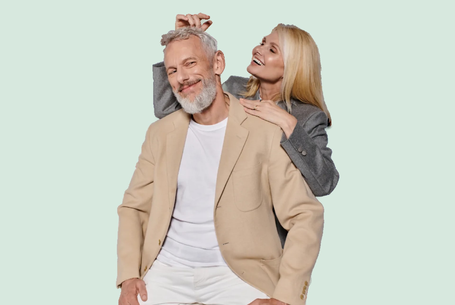 A gray haired man in a cream blazer and a blonde woman laughing behind him