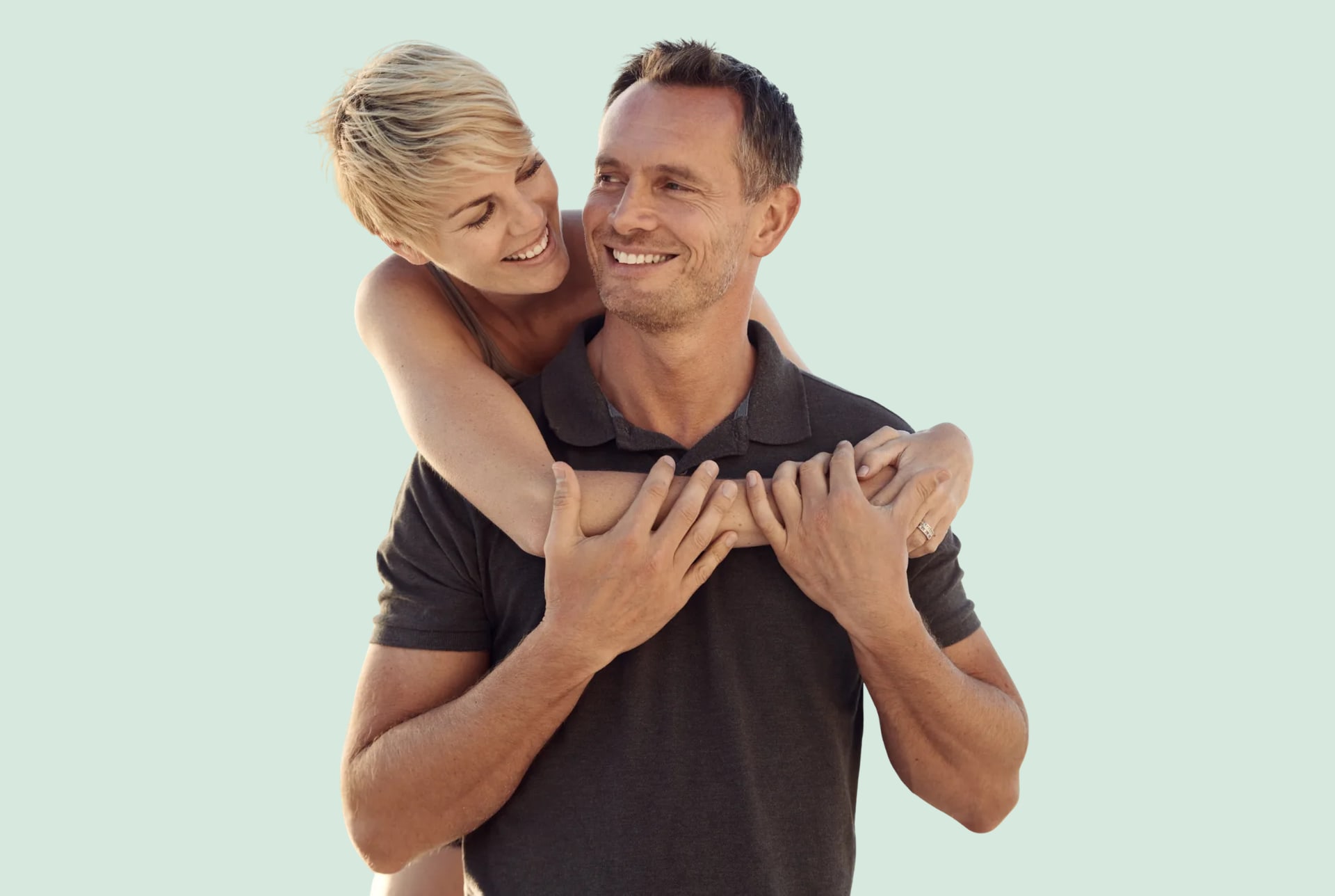 A woman hugging a smiling man from behind