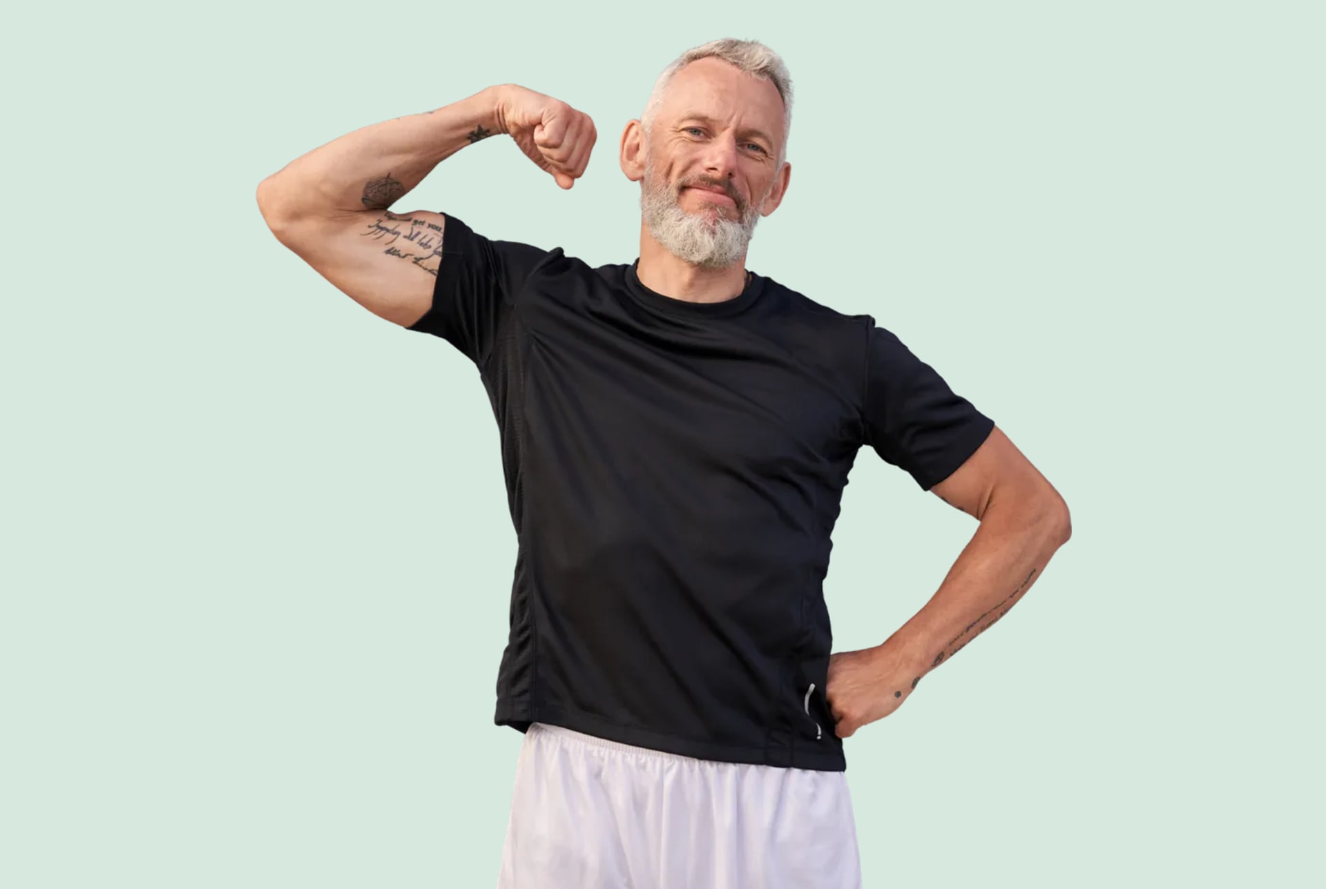A gray bearded man flexing his arm in a black t-shirt, smiling